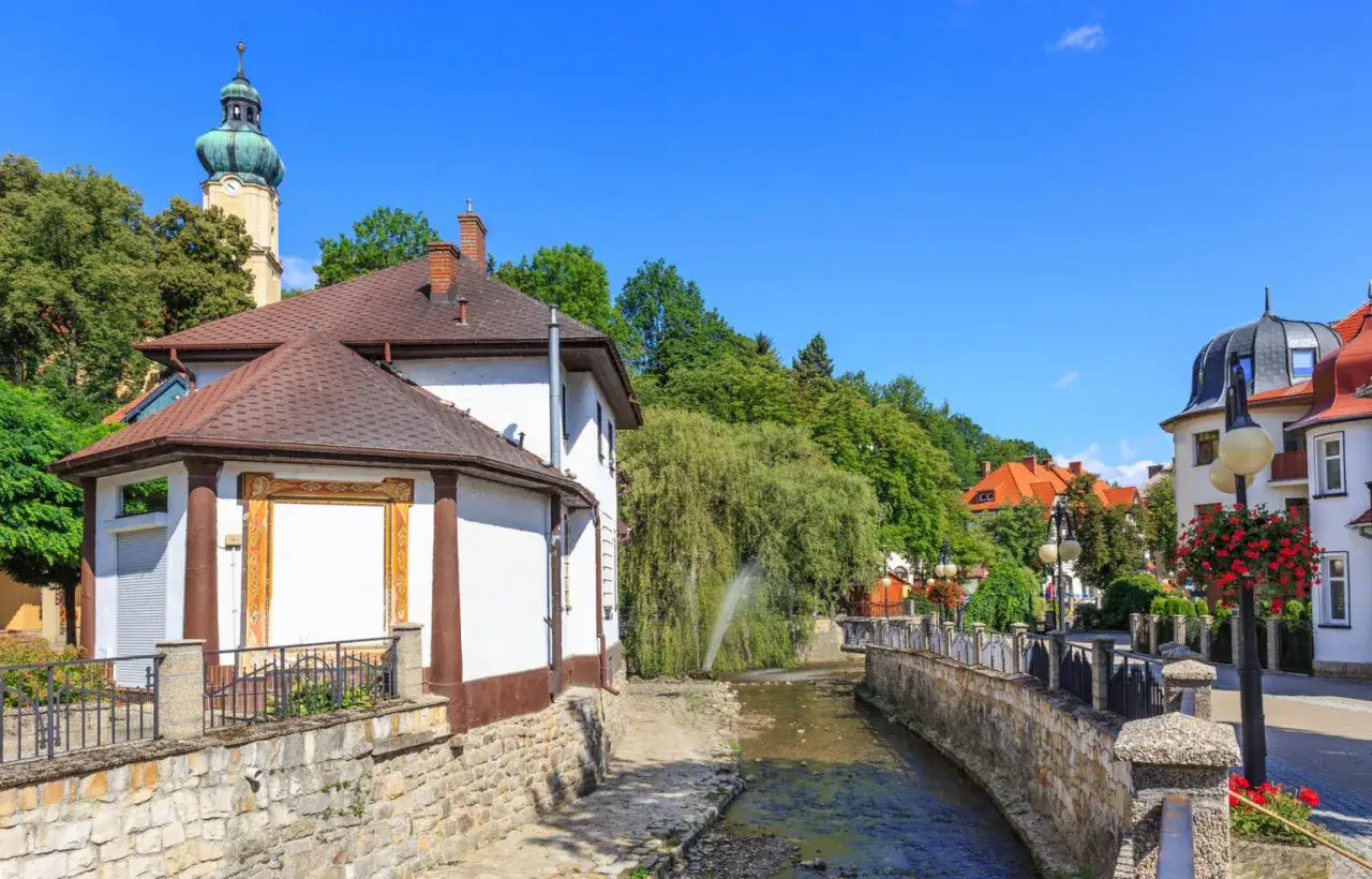 Widok na Polanicę-Zdrój z rzeką, budynkami i wieżą kościelną.